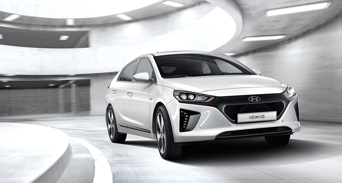 Side front view of white Ioniq electric driving in the car park tower